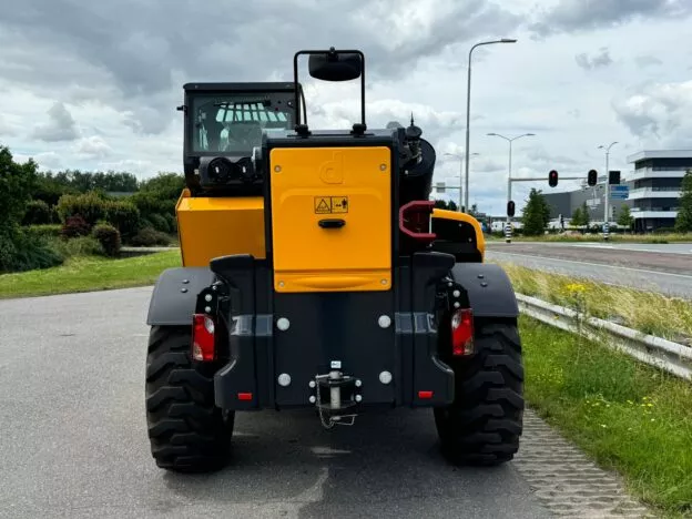 Rear view of a yellow construction vehicle with large tires, parked on a road near a grassy area and traffic lights.