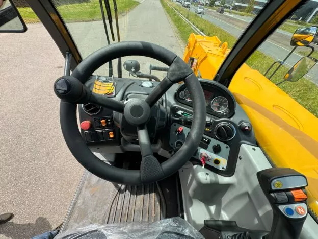 Close-up of a construction vehicle's steering wheel and control panel with various buttons and a digital display.