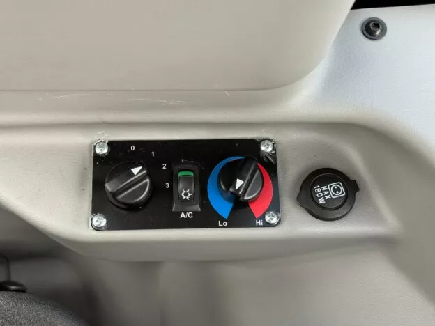 Close-up of vehicle climate control panel with air conditioning, temperature settings, and power outlet.