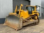 Yellow Caterpillar bulldozer D8T positioned outside a commercial building, showcasing its tracked wheels and large front blade.