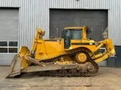 Yellow CAT D8T bulldozer parked in front of an industrial building with closed garage doors.