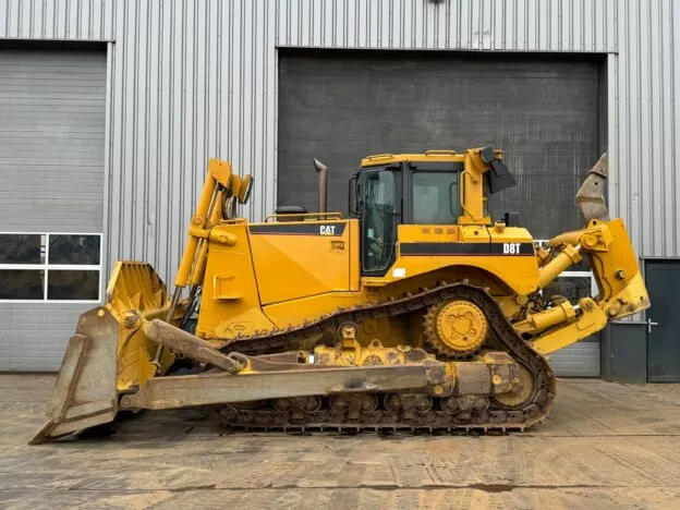 Yellow CAT D8T bulldozer parked in front of an industrial building with closed garage doors.