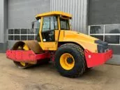 Yellow and red road roller compactor parked outside a modern industrial building for construction and paving jobs.