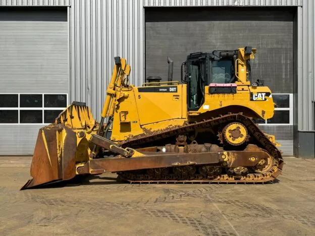 Yellow Caterpillar D8T bulldozer parked outdoors, near industrial building. Ideal for heavy construction and earth-moving tasks.