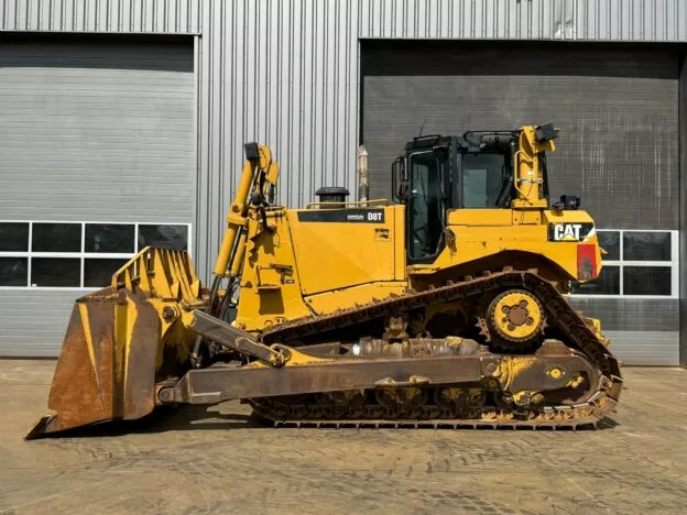 Yellow CAT D8T bulldozer in front of a metal building with a closed garage door, ready for construction use.