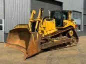 Yellow Caterpillar D8T bulldozer parked outside an industrial building on a sunny day.