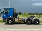 Blue semi-truck parked on the roadside with a cloudy sky in the background, ready for transportation.