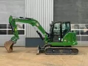 Green Caterpillar mini excavator parked in front of an industrial building with metal siding and windows.