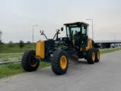 Yellow Hyundai road grader parked on an asphalt road beside green grass and street lamps, ready for construction work.