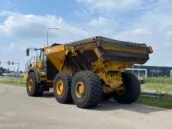 Yellow Bell dump truck parked near road with clear sky background, next to Everest Fresh building.