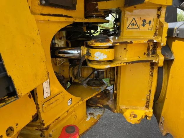 Close-up of a yellow industrial machine part with hydraulic components and safety warning stickers visible.