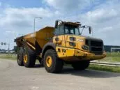 Yellow Bell B45E articulated dump truck parked on a road with a cloudy sky in the background.